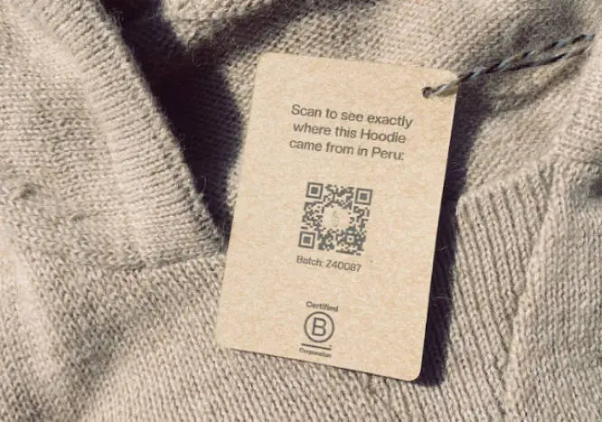 Close-up of a hoodie hang tag showcasing a QR code and the text ‘Scan to see exactly where this Hoodie came from in Peru’ on knit fabric