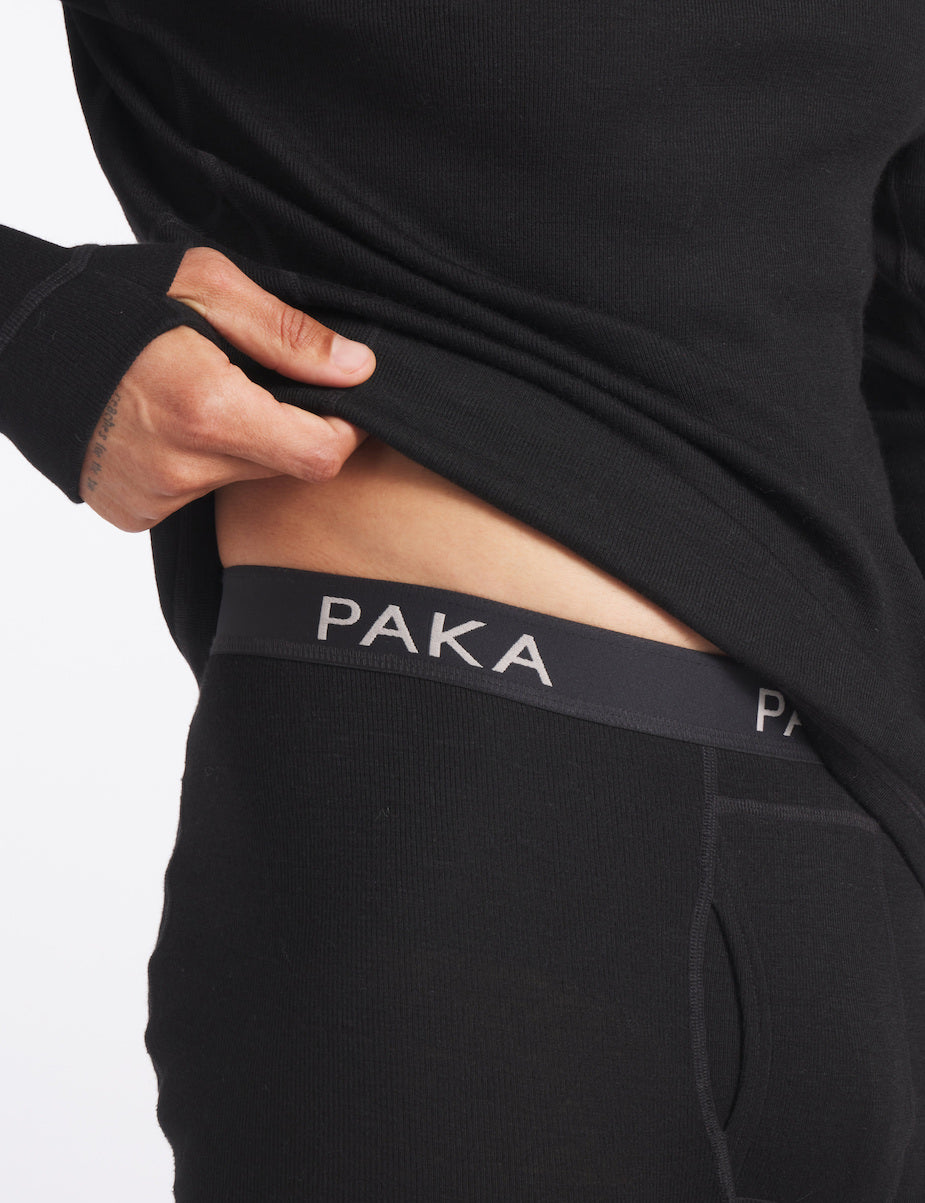 Waist-level close view of men’s thermal baselayer bottoms showcasing PAKA elastic waistband and front fly on black fabric