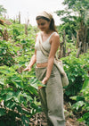Woman standing in a lush Peruvian forest wearing a light beige tank, loose beige pants, a cap, and a shoulder bag