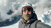 Climber in helmet, goggles, and insulated jacket taking a selfie on snowy Yanapaccha with cloudy peaks behind