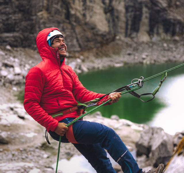A smiling man climbing the Andes mountains wearing a red insulating Pakafill Jacket