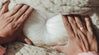 Close-up of hands holding raw white alpaca wool showing soft fluffy unspun fiber on a woven blanket background