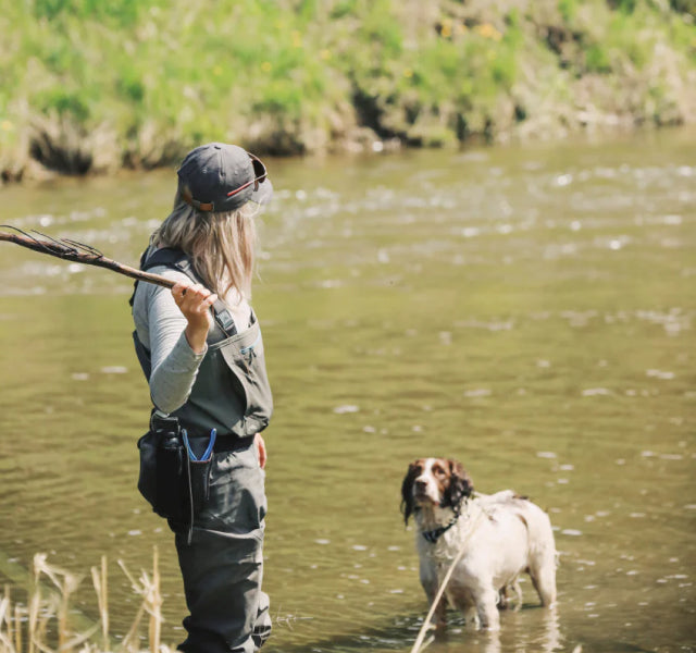 A woman wearing a lightweight baselayer alpaca shirt having fun with a white dog in a river