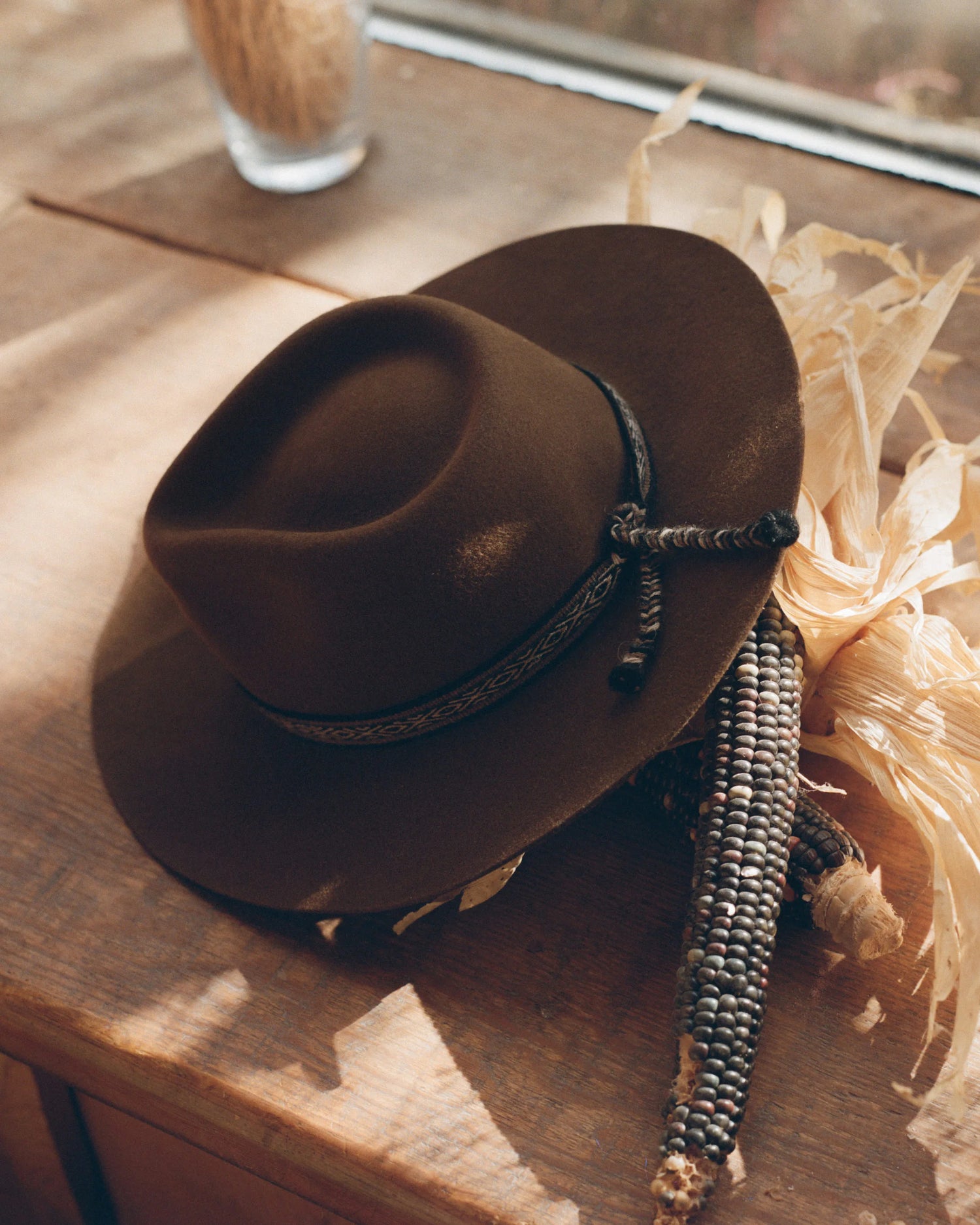 Angled top view of Alpaquero Hat showcasing molded crown, wide brim, and braided hatband with woven tassel on wooden surface