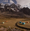 Two tents pitched at a high-altitude campsite beneath snow-capped Ausangate peaks with an overcast sky