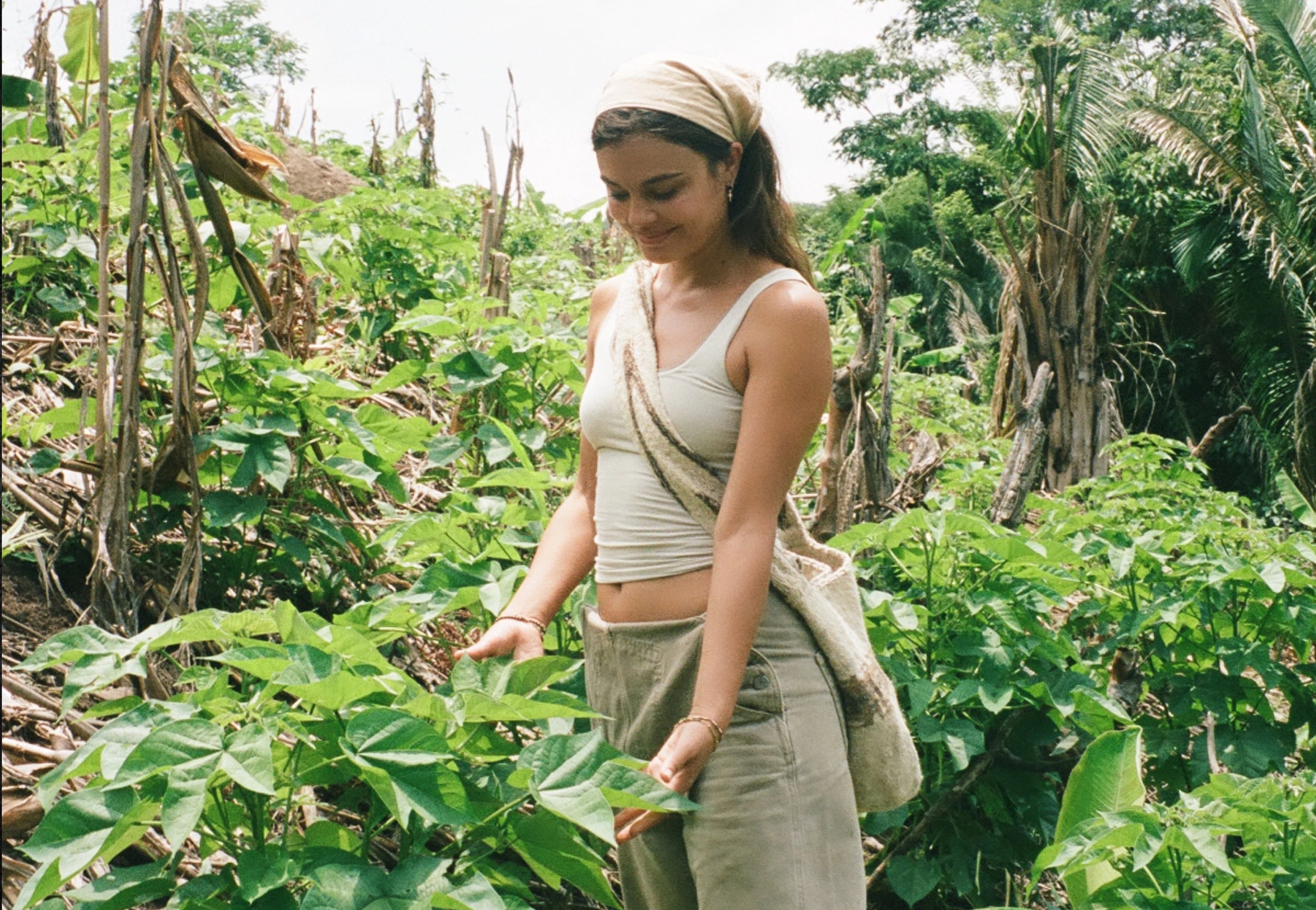 Woman standing in lush Peruvian vegetation wearing a light beige dress and crossbody bag