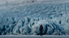 Wide glacial landscape with ice ridges and deep crevasses under an overcast sky