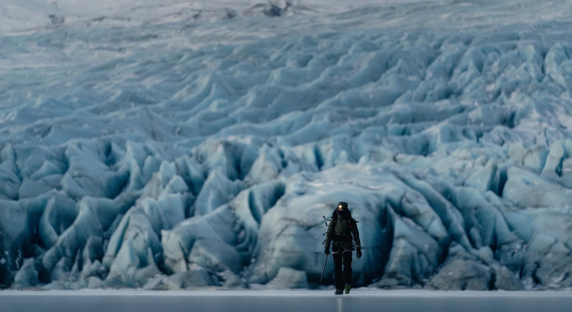 Wide glacial landscape with ice ridges and deep crevasses under an overcast sky