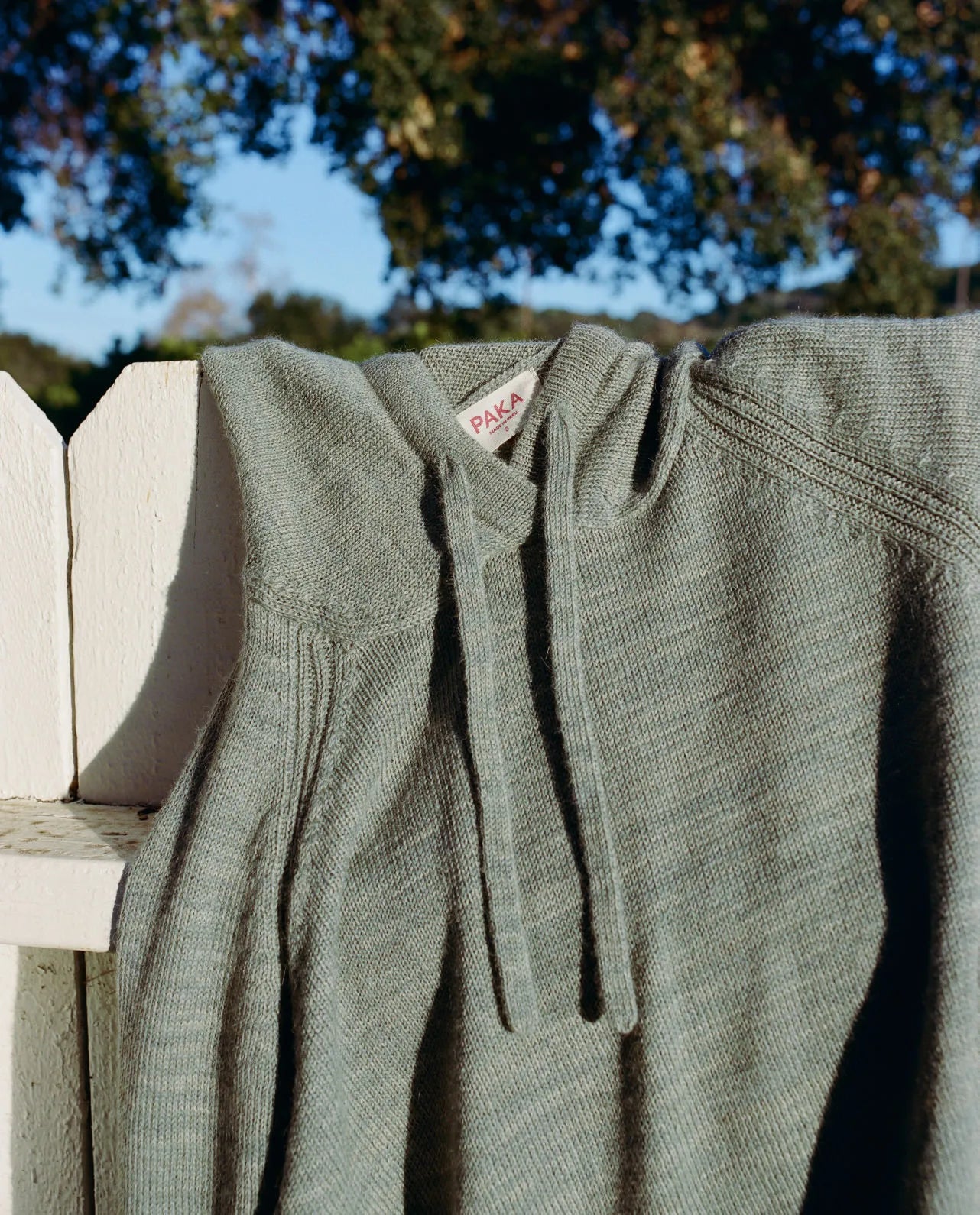 Close-up of women’s alpaca hoodie showcasing soft knit texture, hood, and drawstrings on a white fence outdoors