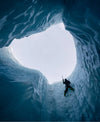 Climber ascending a vertical ice moulin inside a glacier, seen from deep within the blue ice