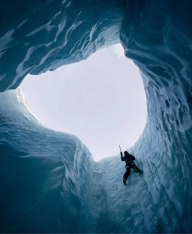Climber ascending a vertical ice moulin inside a glacier, seen from deep within the blue ice