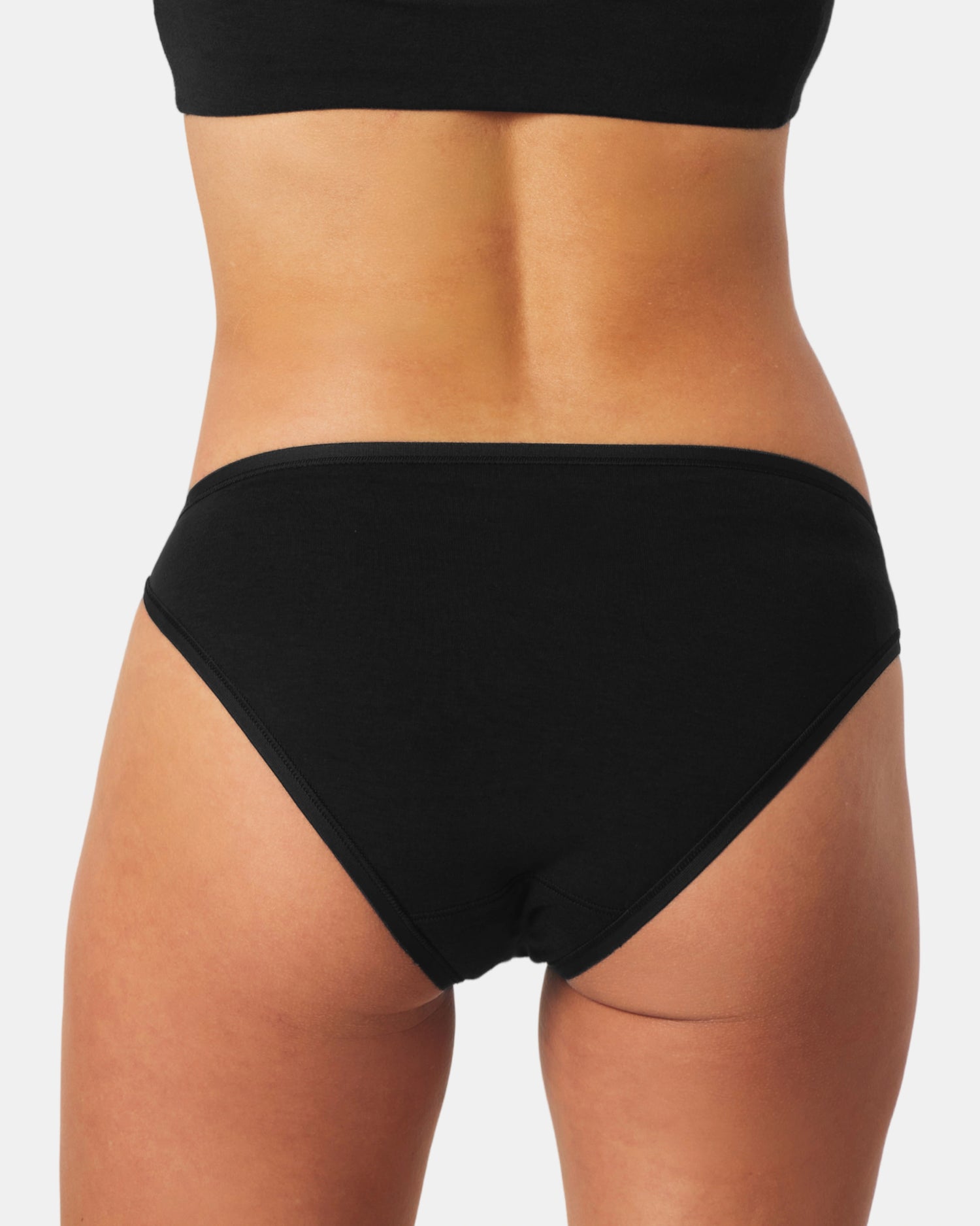 Black bikini bottom worn by a person on a white background