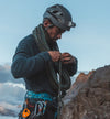 Climber adjusting rope on a rocky slope wearing a dark ultralight crew midlayer and helmet at dawn