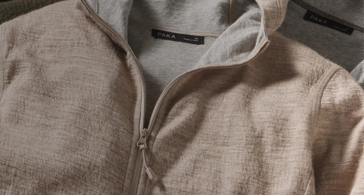 Close-up of Men’s Breathe full-zip hoodie showing the zipper, stand collar, and heathered beige alpaca-knit texture on a flat lay background
