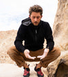 Model wearing black Breathe alpaca zip hoodie crouching on rocky outdoor trail, slim athletic fit