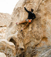 Climber scaling a sunlit rock face wearing a black zip hoodie and orange shorts