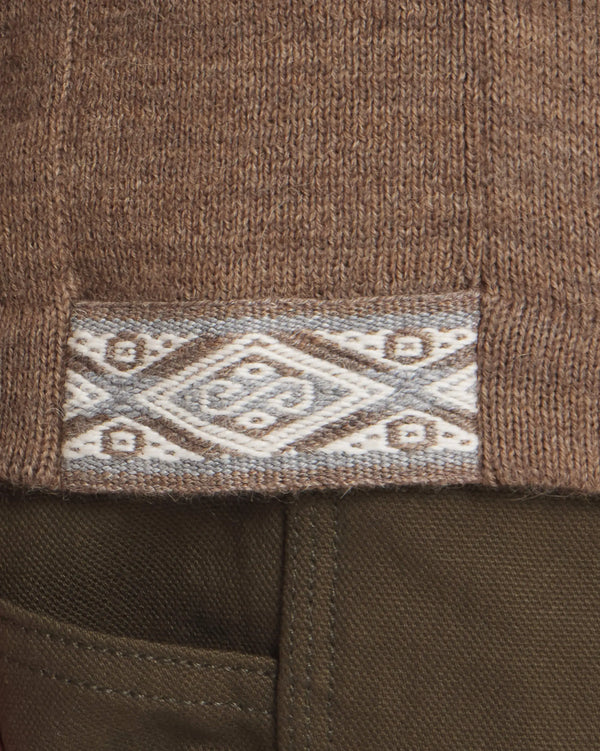 Close-up of The Hoodie alpaca sweater hem showcasing woven diamond-pattern trim above an olive pant pocket