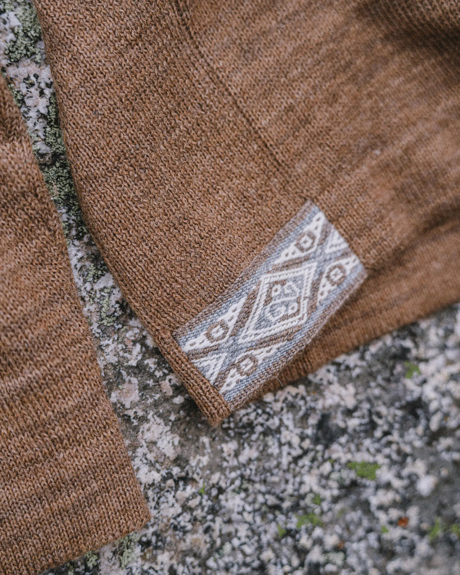 Close-up of The Hoodie sweater hem showcasing woven patterned cuff on café heather knit against lichen-covered stone