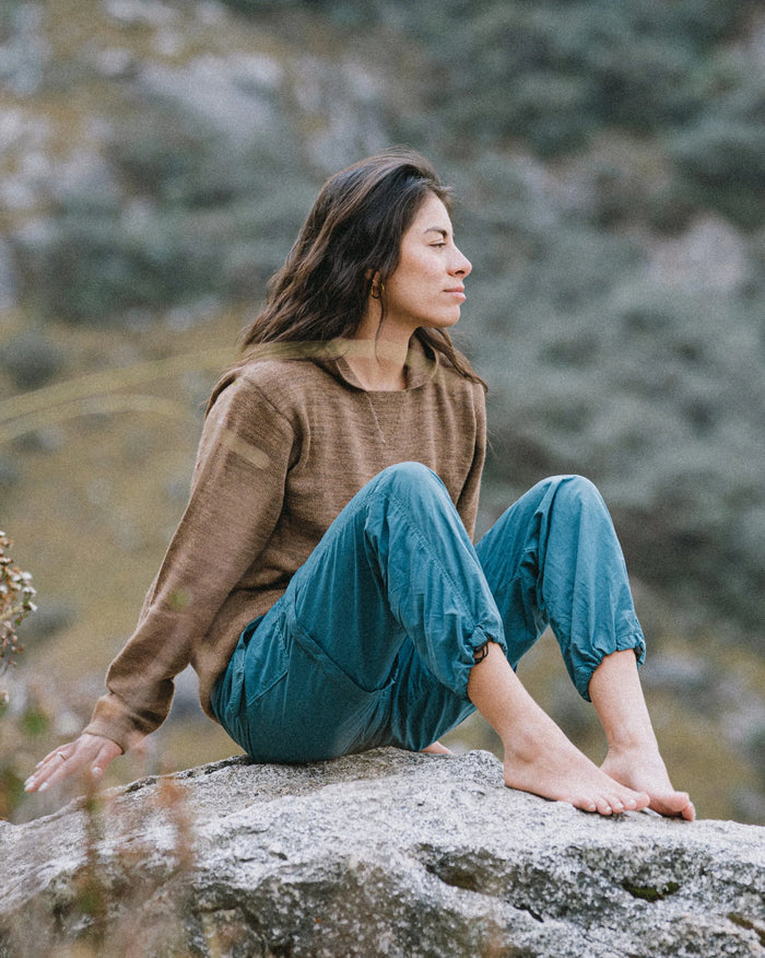 Woman seated on a rock wearing a cafe heather unisex alpaca hoodie, relaxed outdoors in a rocky setting