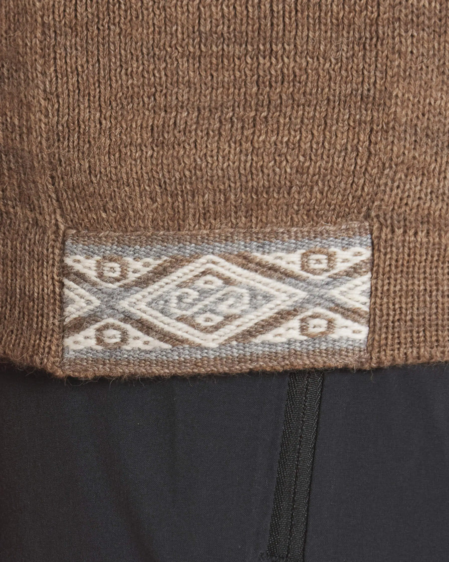 Close-up of The Original Crew sweater hem in brown showing woven diamond trim and ribbed knit over black pants
