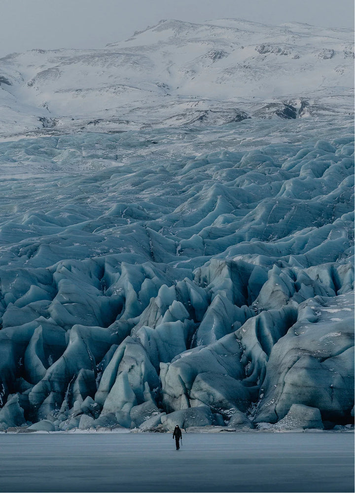 Person ice climbing on a blue glacier in Iceland using crampons and ice axes