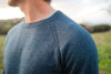 Close-up of men’s blue ultralight alpaca crew sweater showing raglan shoulder and fine knit with blurred outdoor background