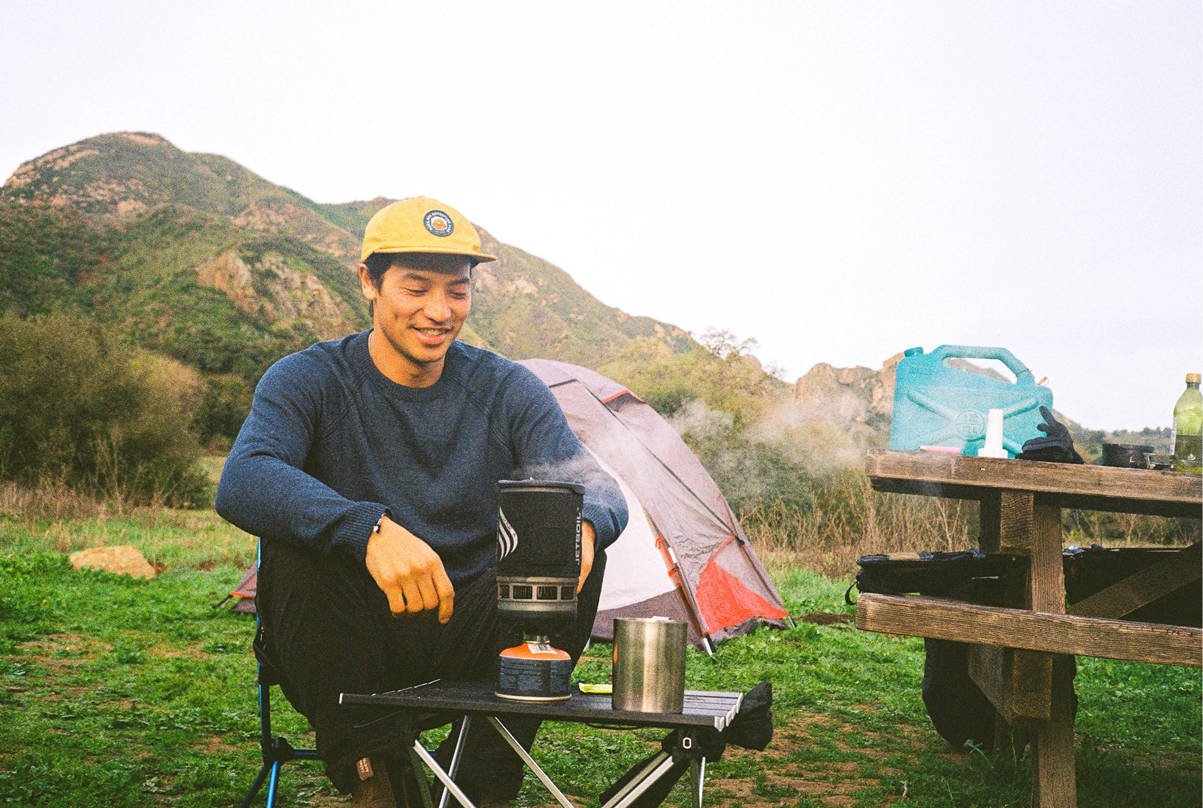 Man wearing a navy ultralight alpaca sweater sitting on a picnic bench in a sunny mountain meadow