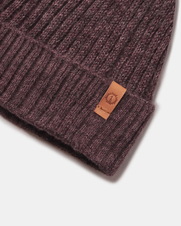 Close-up of Raisin Marl beanie showing ribbed cuff, fuzzy alpaca-blend knit and leather logo tab on light gray