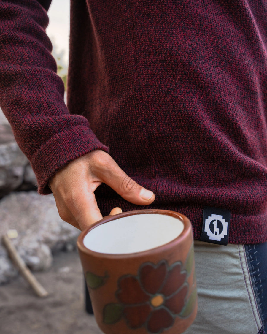 Close-up of The Cusco burgundy sweater showing marled alpaca-merino knit and mock roll neckline as model holds a mug outdoors