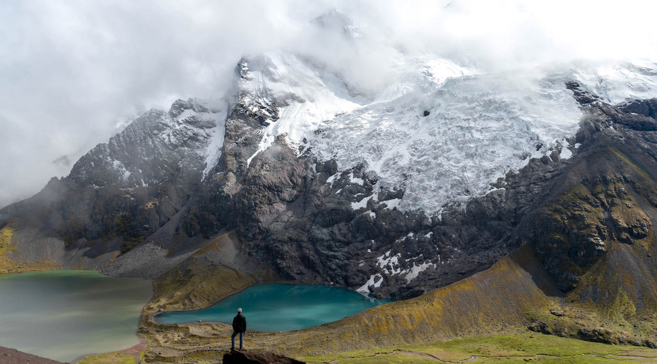 Hiker standing in front of a blue glacial lake at Ausangate
