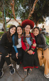 Nohemi Mamani Puma standing with four women outdoors, wearing a red traditional hat and woven shawl, smiling