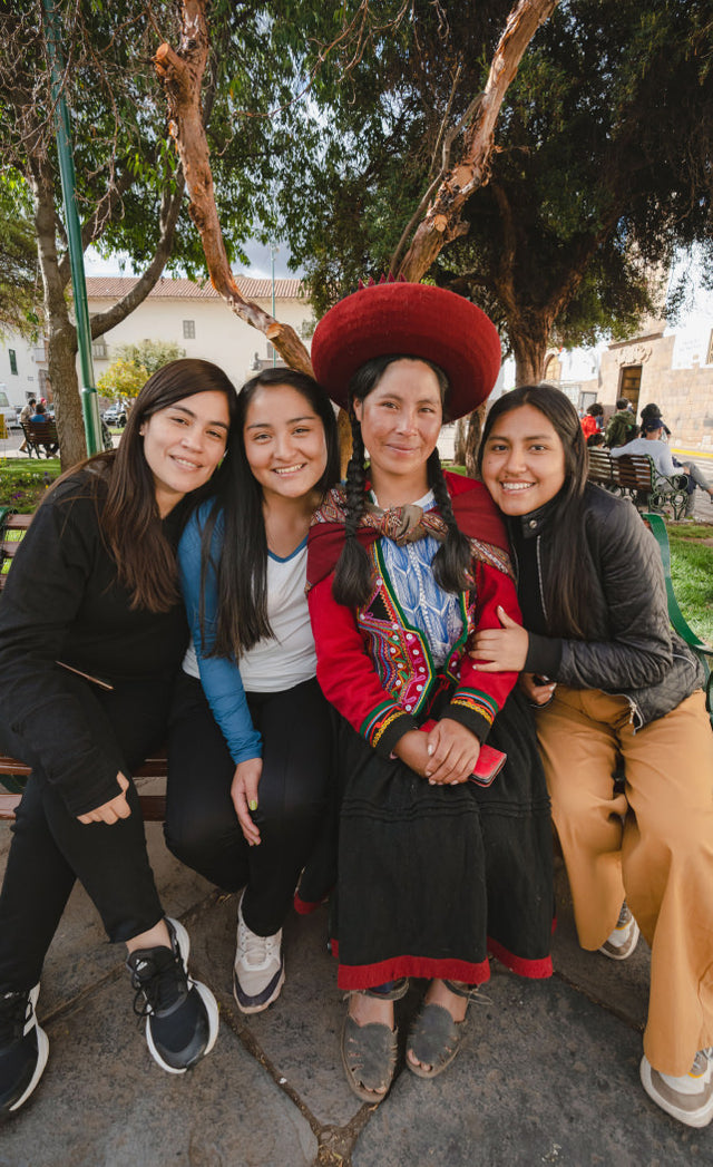 Nohemi Mamani Puma standing with four women outdoors, wearing a red traditional hat and woven shawl, smiling