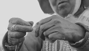 Close-up of a person’s hands tying a small knot on a cord, outdoor clothing visible in the background