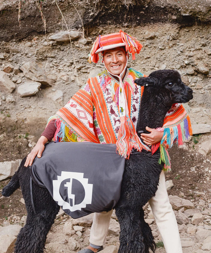 Person in colorful traditional Andean clothing posing with an alpaca on a rocky hillside