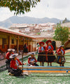 Quechua weavers in colorful traditional dress seated in a courtyard with handmade textiles and Andes mountains in the background