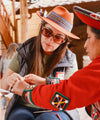 Woman in a hat and sunglasses smiling and interacting with a local child during a PAKA team visit in Cusco, Peru