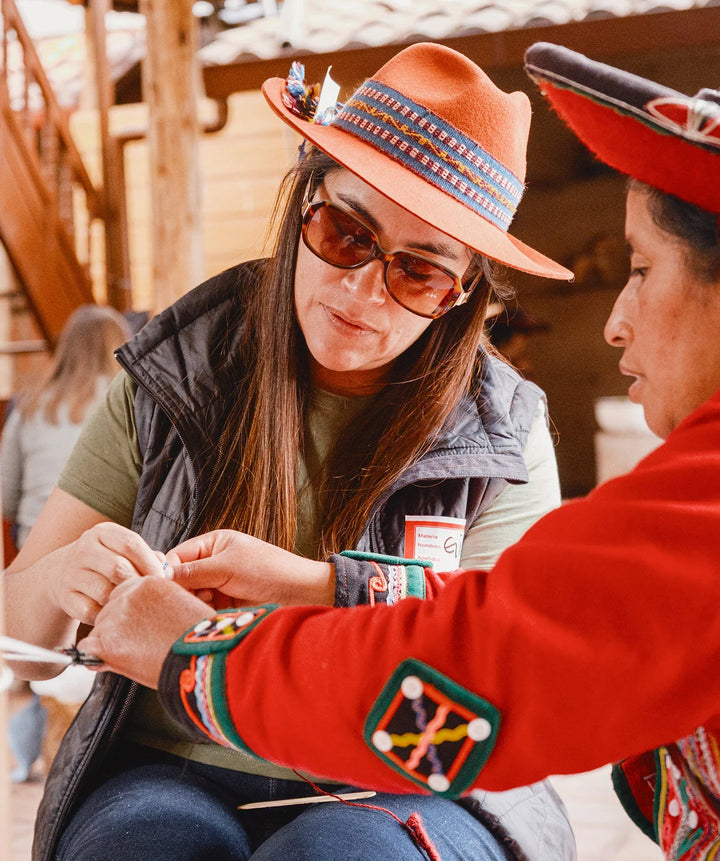 Woman in a hat and sunglasses smiling and interacting with a local child during a PAKA team visit in Cusco, Peru