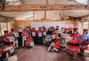 Peruvian weavers seated in a workshop holding colorful textiles and numbered signs, showcasing community artisanship
