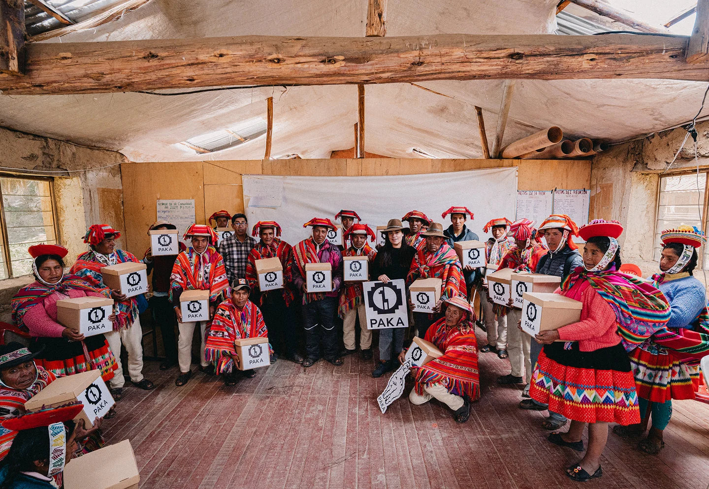 Peruvian weavers seated in a workshop holding colorful textiles and numbered signs, showcasing community artisanship