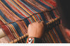 Close-up of hands weaving a multicolored striped Peruvian textile on a loom, highlighting traditional weaving techniques