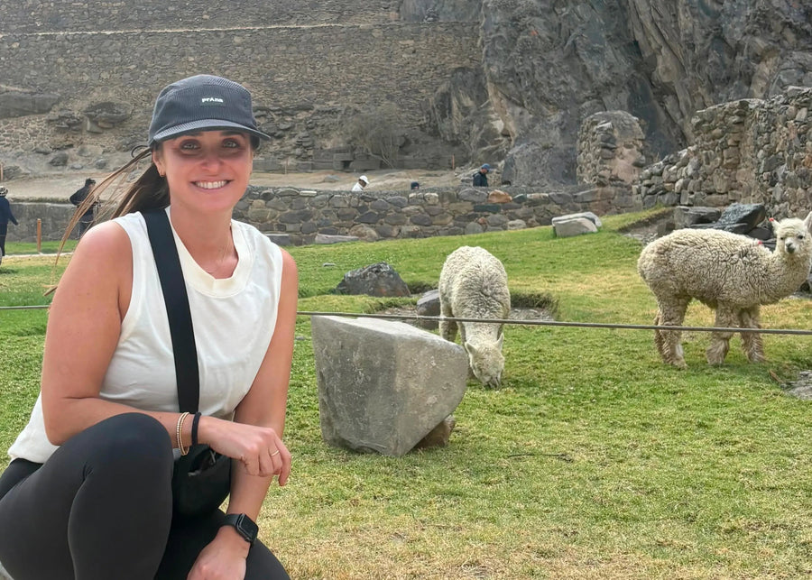 Woman posing with llamas in a grassy area with stone ruins in the background