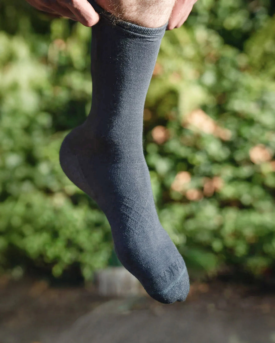 On foot view of Essential Crew Socks showcasing indigo alpaca wool crew length with blurred outdoor background