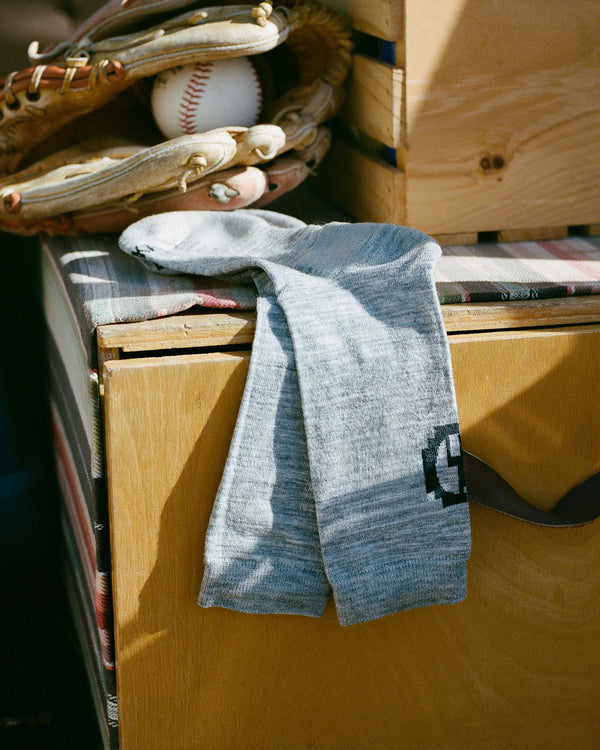 Essential Crew Socks in light grey draped over a wooden crate showing alpaca knit texture with baseball glove and ball