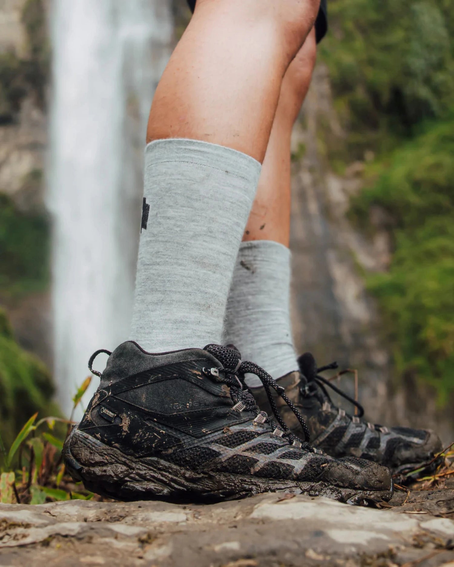 Side view of Essential Crew Socks in light gray on a hiker, showing mid-calf fit and alpaca knit texture by a waterfall