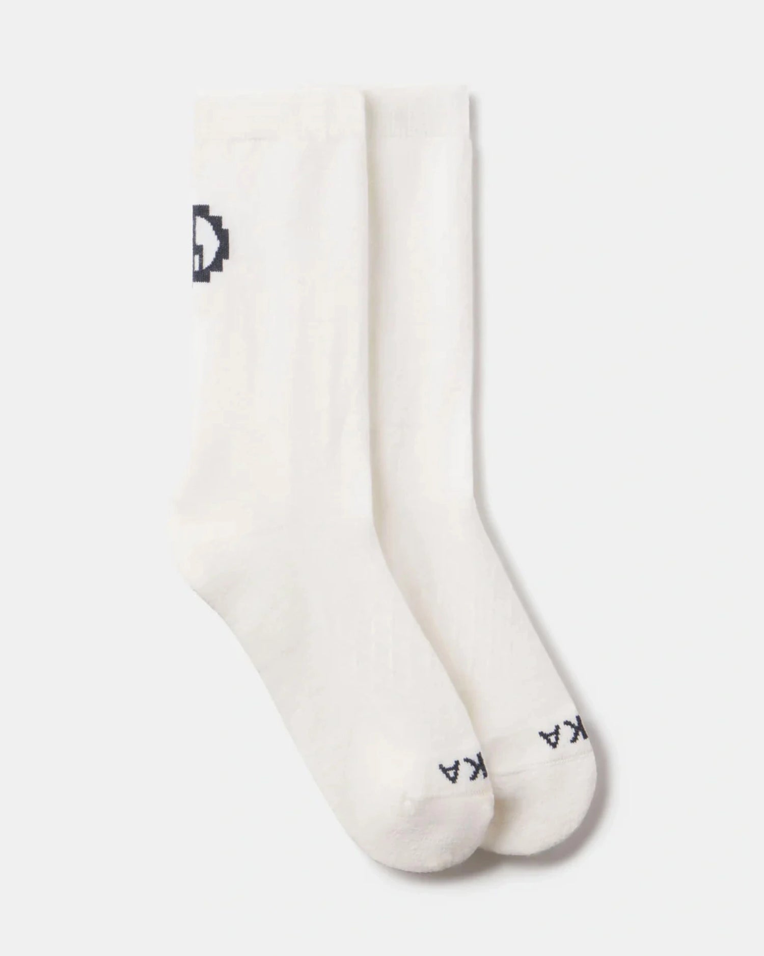 Top view of Essential Crew Socks showcasing white alpaca crew socks with black PAKA logo at toe and cuff on light gray background