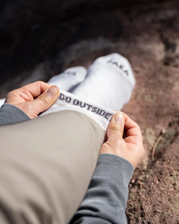 Close-up of Essential Crew Socks (alpaca) with top rolled to reveal GO OUTSIDE interior branding on rocky ground