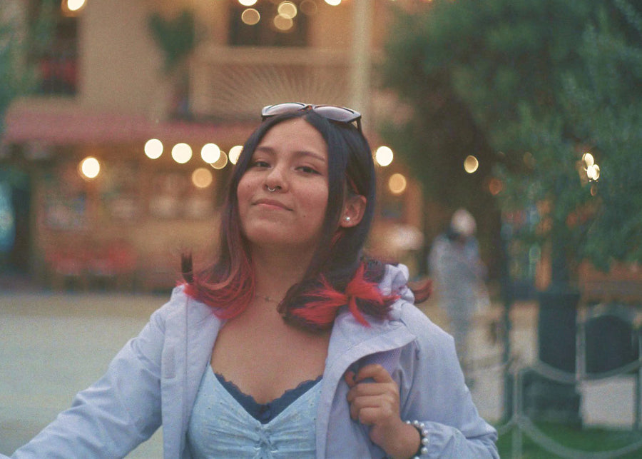 Woman with colorful hair and sunglasses on head, standing outdoors with blurred background