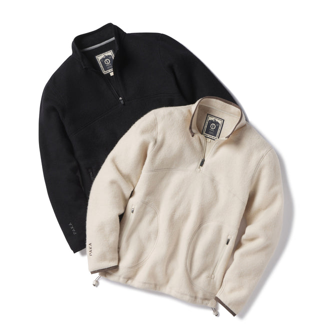 Flat-lay of two PAKACLOUD quarter-zip fleeces (black, natural) showing alpaca texture, zip pockets and drawcord hem