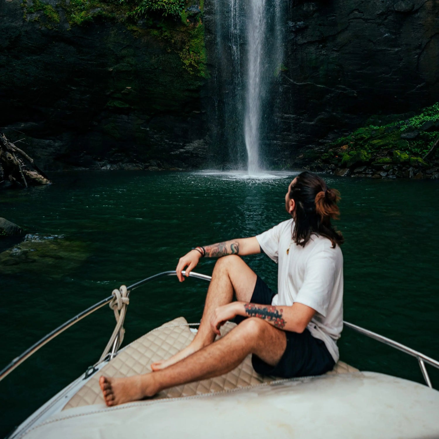 Man Sitting at Bow of Boat Wearing a Cream / White Alpaca T-Shirt in Front of a Waterfall – PAKA Apparel