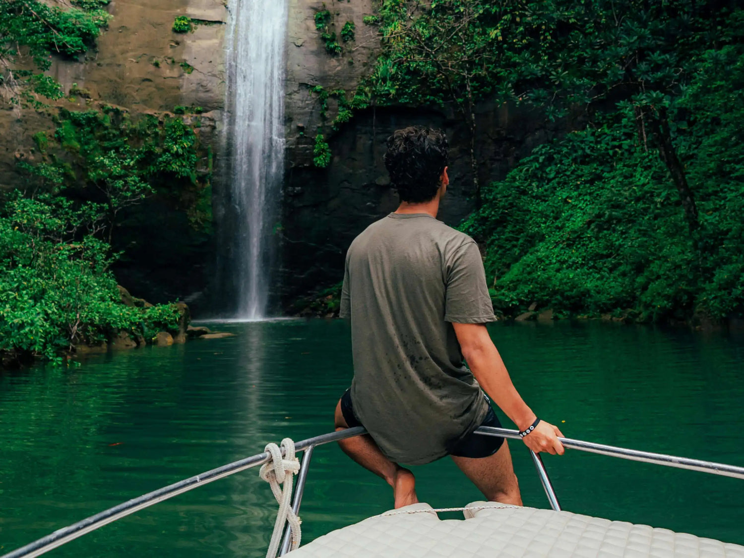 Man on a Boat Wearing a Green Alpaca T-Shirt in Front of a Waterfall and Greenery – PAKA Apparel